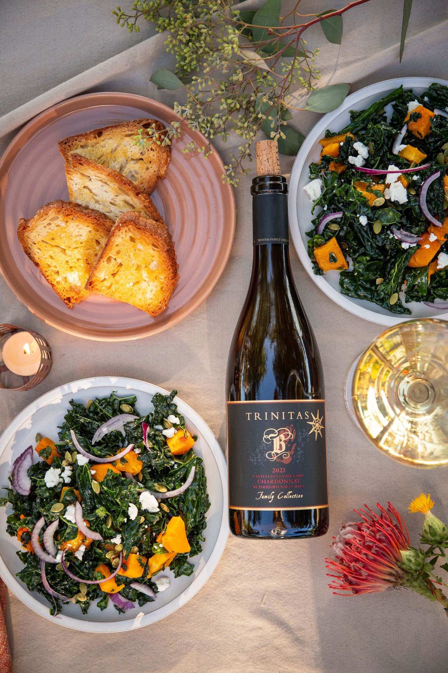 Elegant dinner spread with wine, kale salad, and grilled dishes on pink plates.