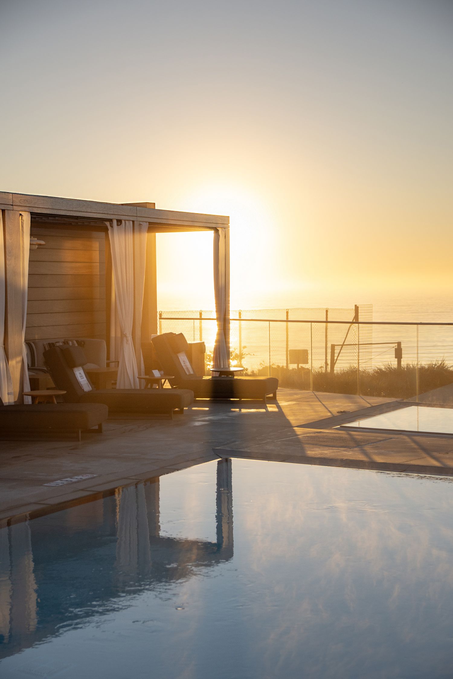 Luxury infinity pool overlooking the ocean at sunset with cabanas.