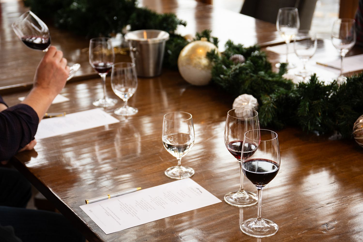 Wine glasses and tasting notes arranged on wooden table with festive greenery.