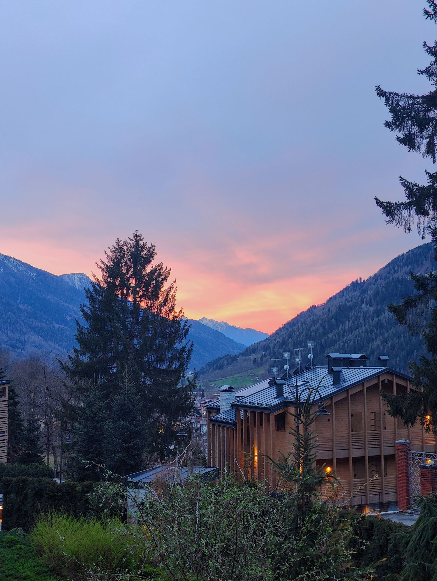 Mountain lodge cabins nestled in pine trees at sunset with pink and purple sky.