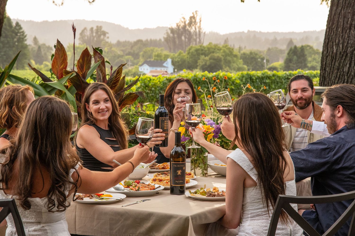 Guests enjoying wine and conversation at outdoor tables with scenic mountain views in the background.