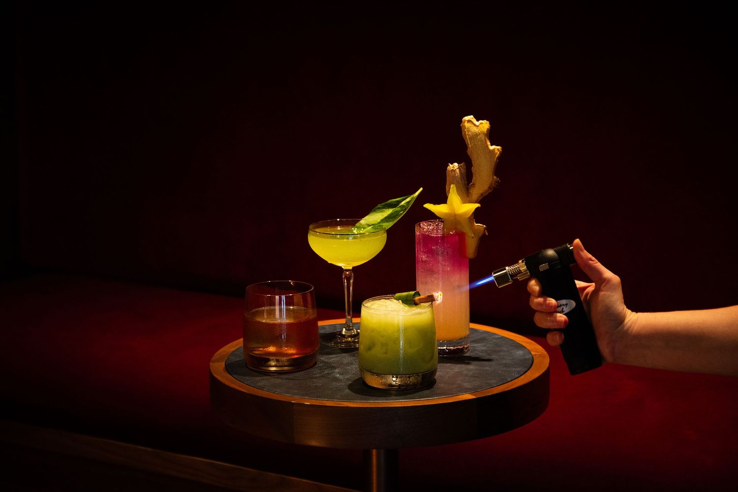 Colorful craft cocktails served on a dark round tray with dramatic lighting.