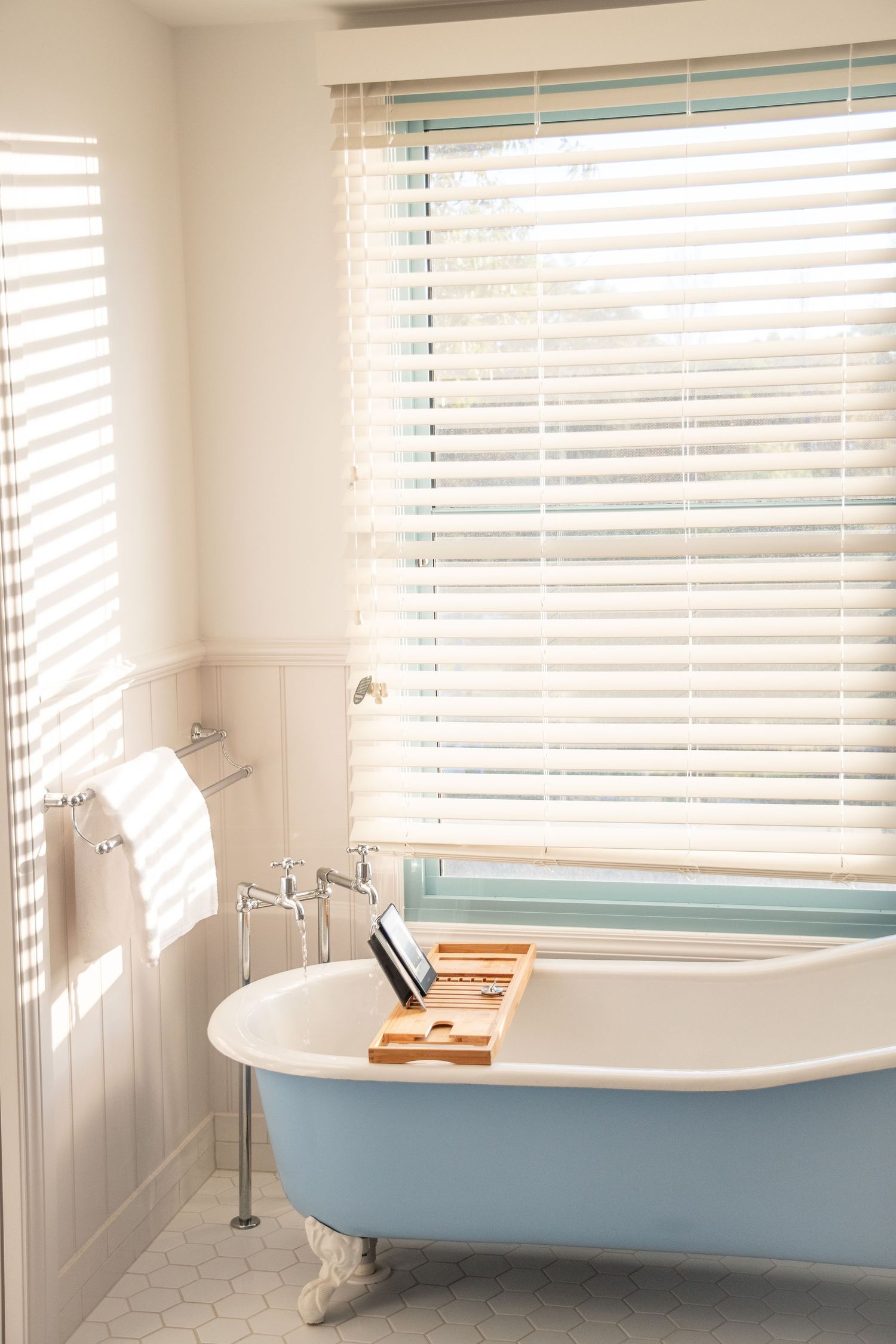 Bright bathroom interior with vintage clawfoot tub and sunlight streaming through venetian blinds.