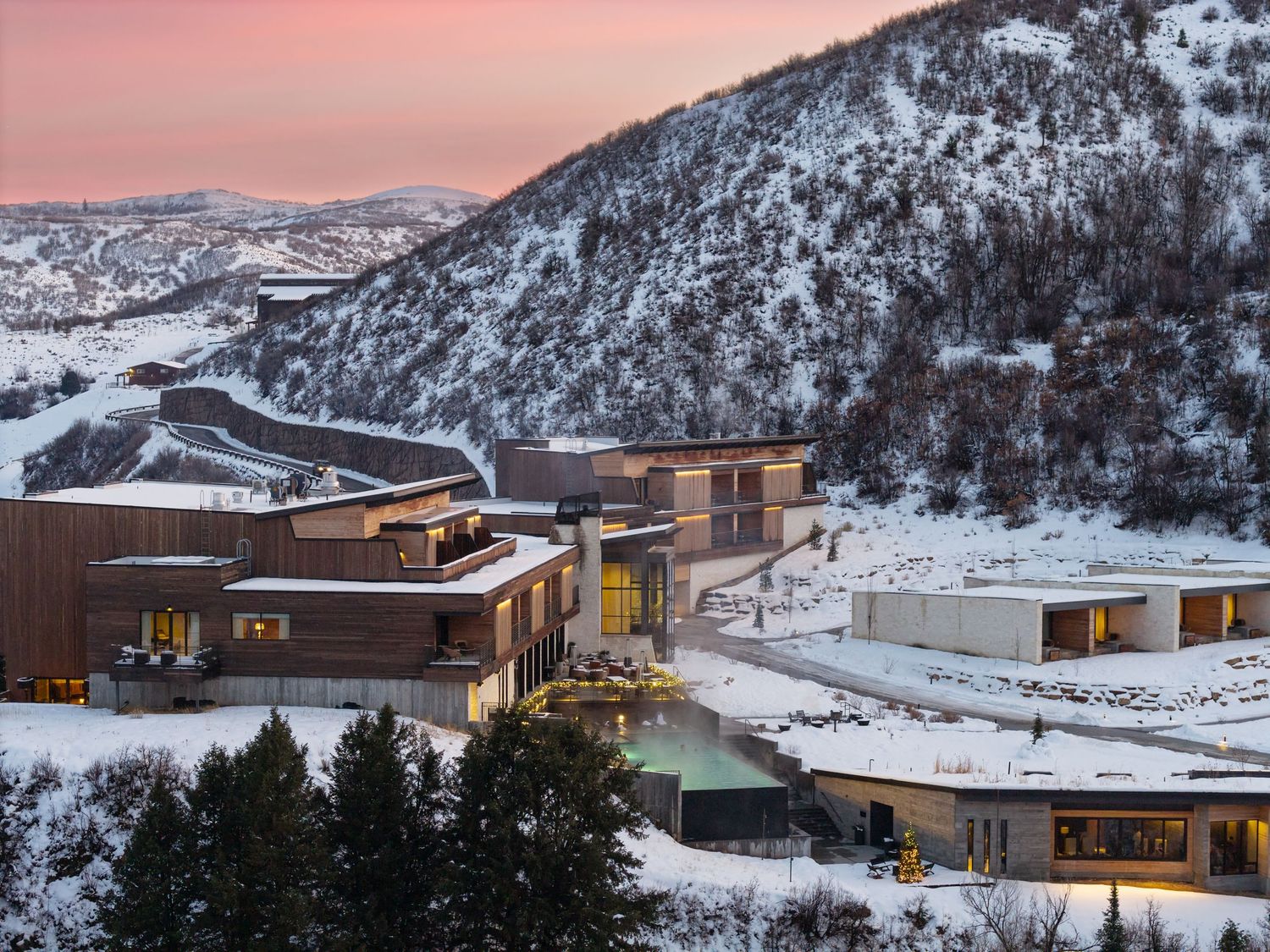 Modern mountain resort buildings nestled in snowy terrain during a pink sunset.
