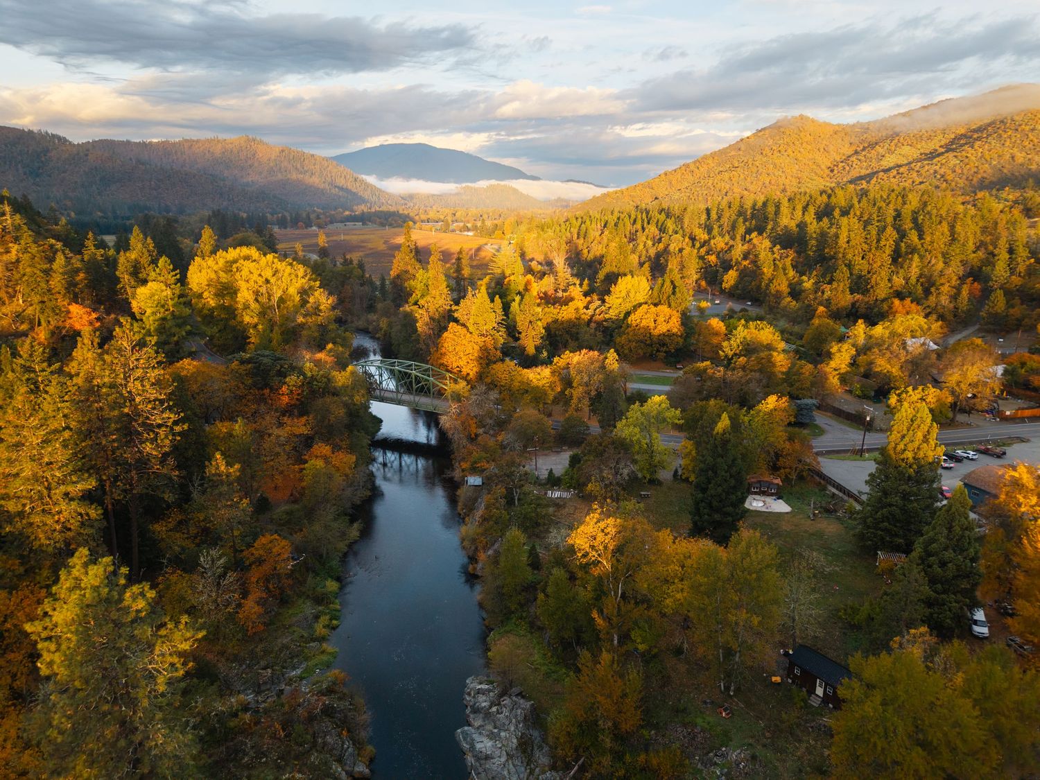 Aerial autumn view of a winding river through colorful fall forest with mountains and misty valley in background.
