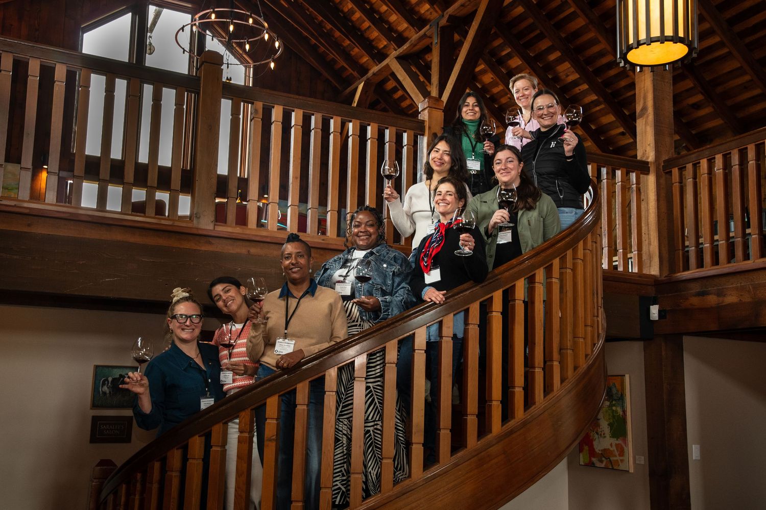 People line the wooden staircase and balcony of a rustic event venue.