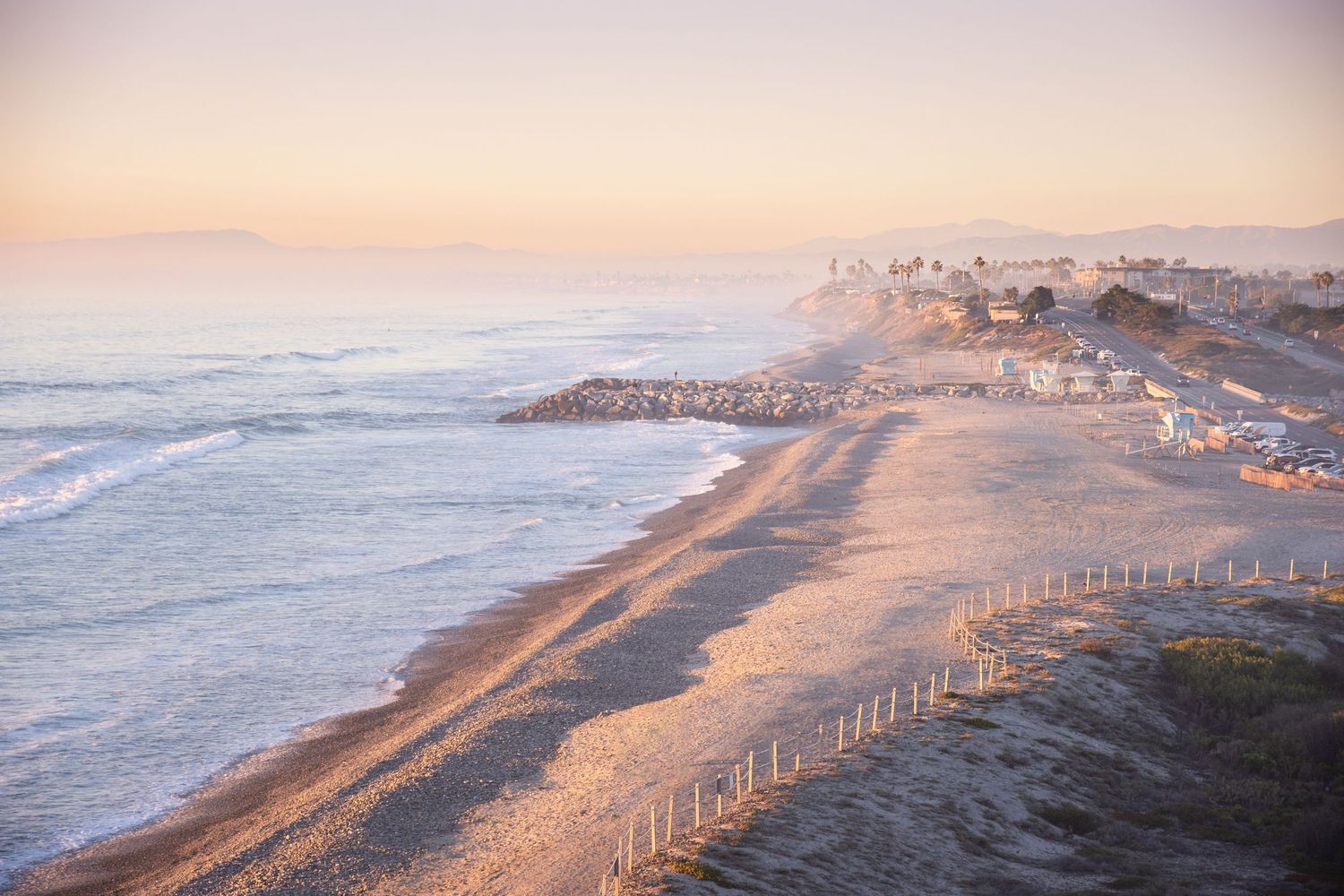 Aerial view of a coastal beach with waves crashing along the shoreline at sunset.