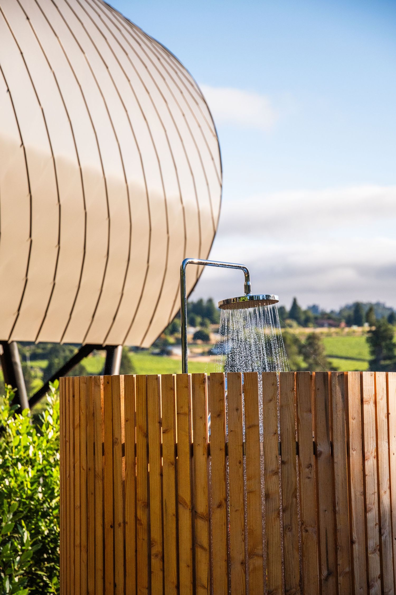 Outdoor shower with wooden privacy fence and curved architectural feature against blue sky.
