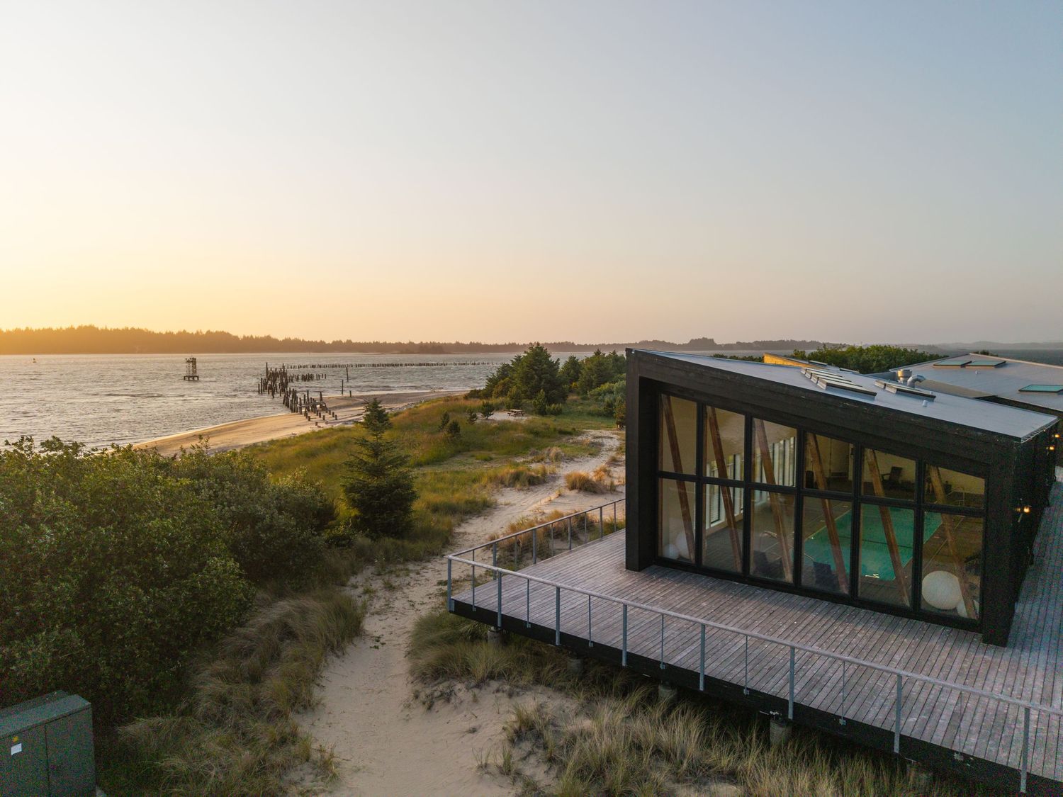 Luxury beachfront cabins with panoramic windows and walkways nestled among coastal dunes.