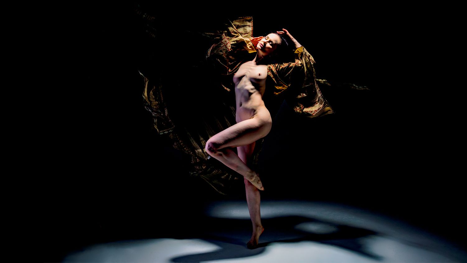 Contemporary dancer strikes a graceful pose with extended limbs in dramatic lighting.