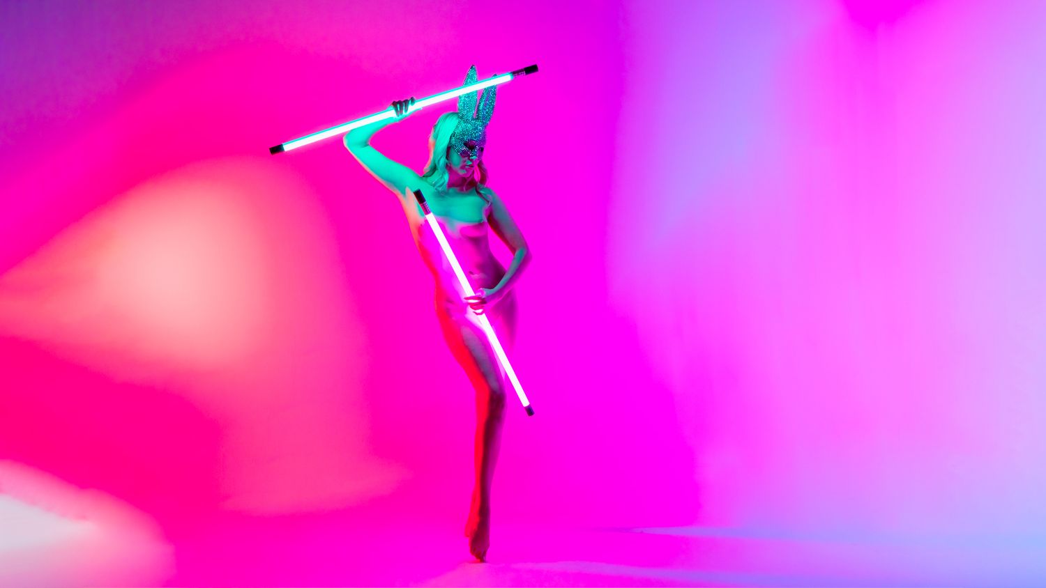 A series of dancers in bright pink lighting strike graceful poses against a vibrant backdrop.