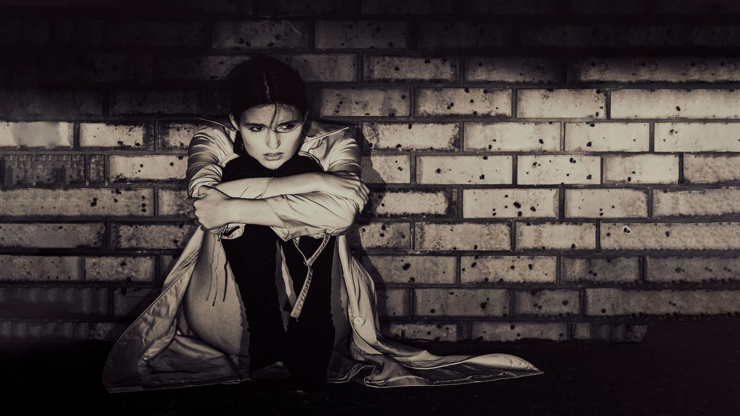Moody portraits against a brick wall background in dark lighting.