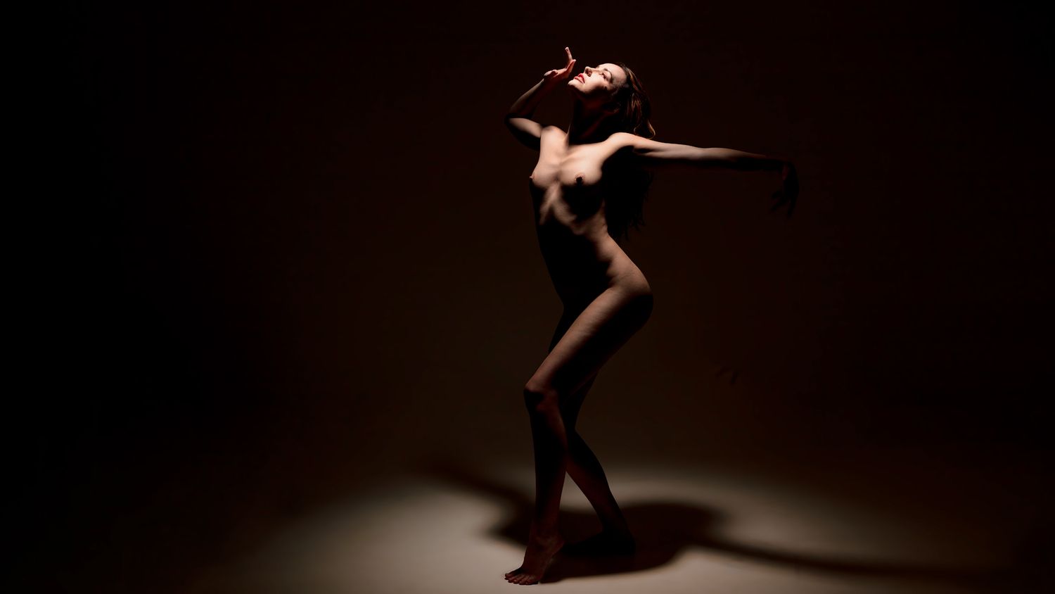 Silhouetted dancer in mid-leap performs an elegant split jump against a dark background.