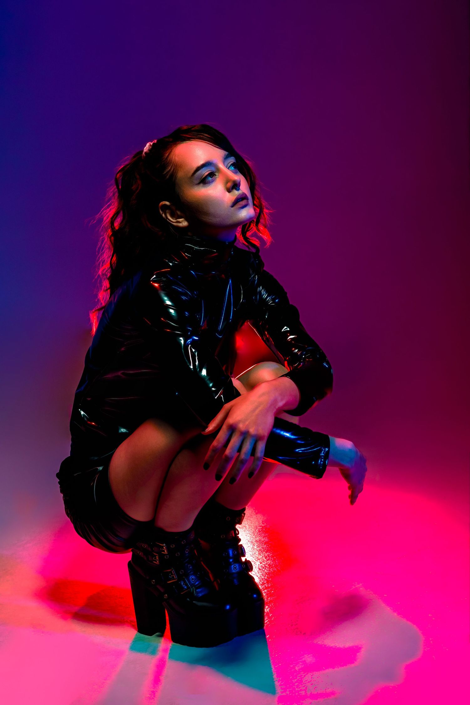 Fashion model poses in black leather outfit against purple and pink lighting.