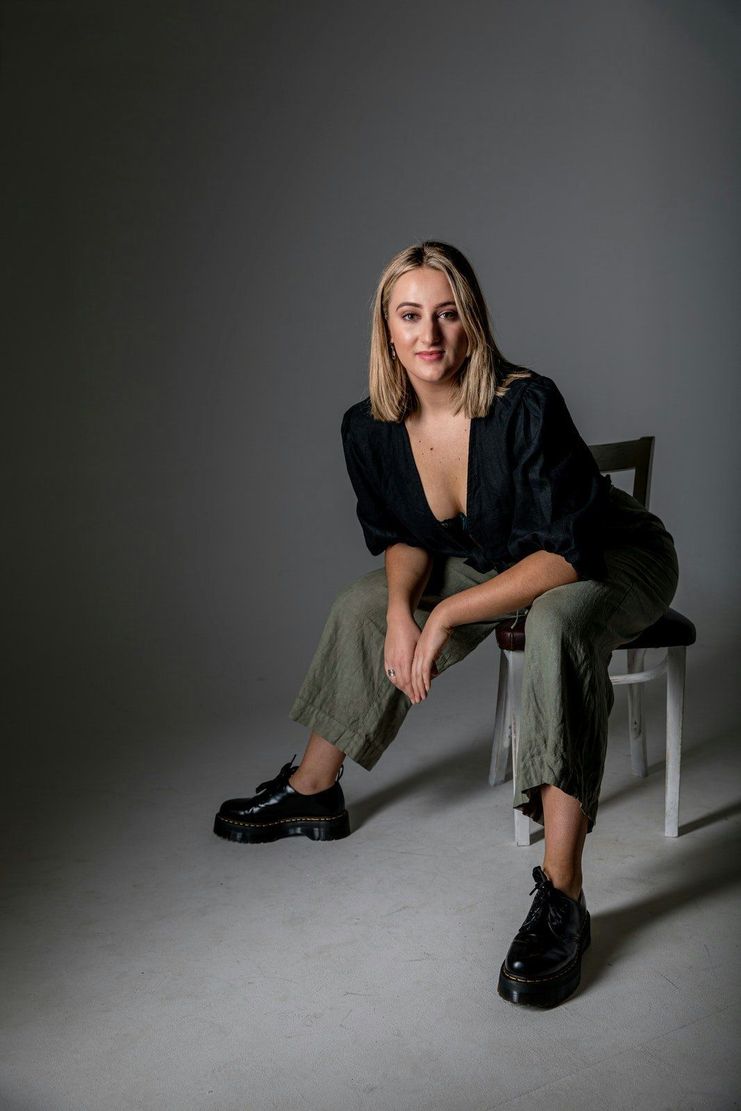 Fashion photoshoot with model in black outfit and combat boots on grey backdrop.