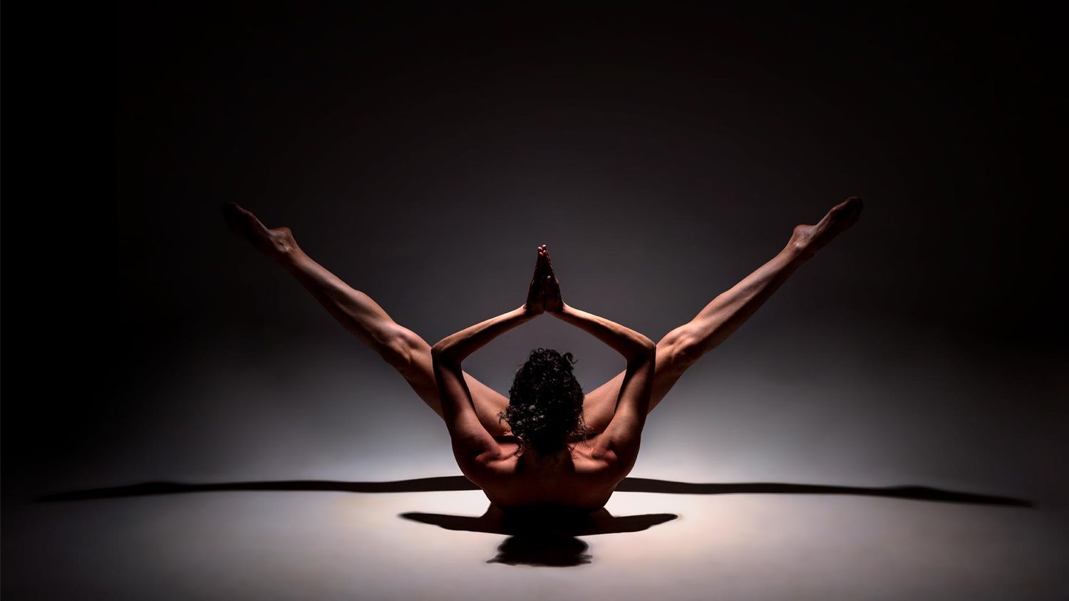 A dramatic silhouette of a dancer in a graceful split pose against a dark background with dramatic lighting.
