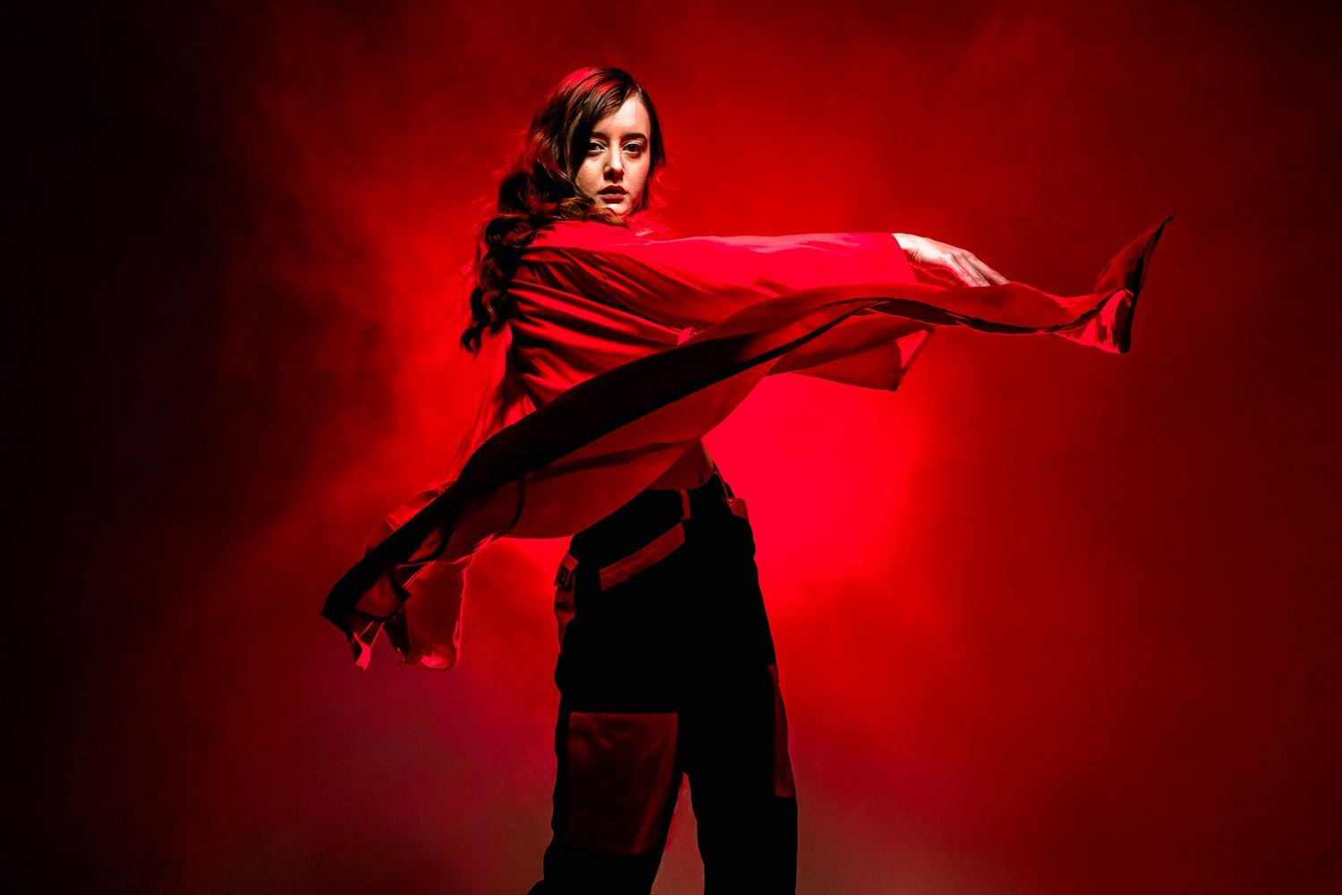 Dramatic fashion photoshoot with figure posing against deep red background lighting.