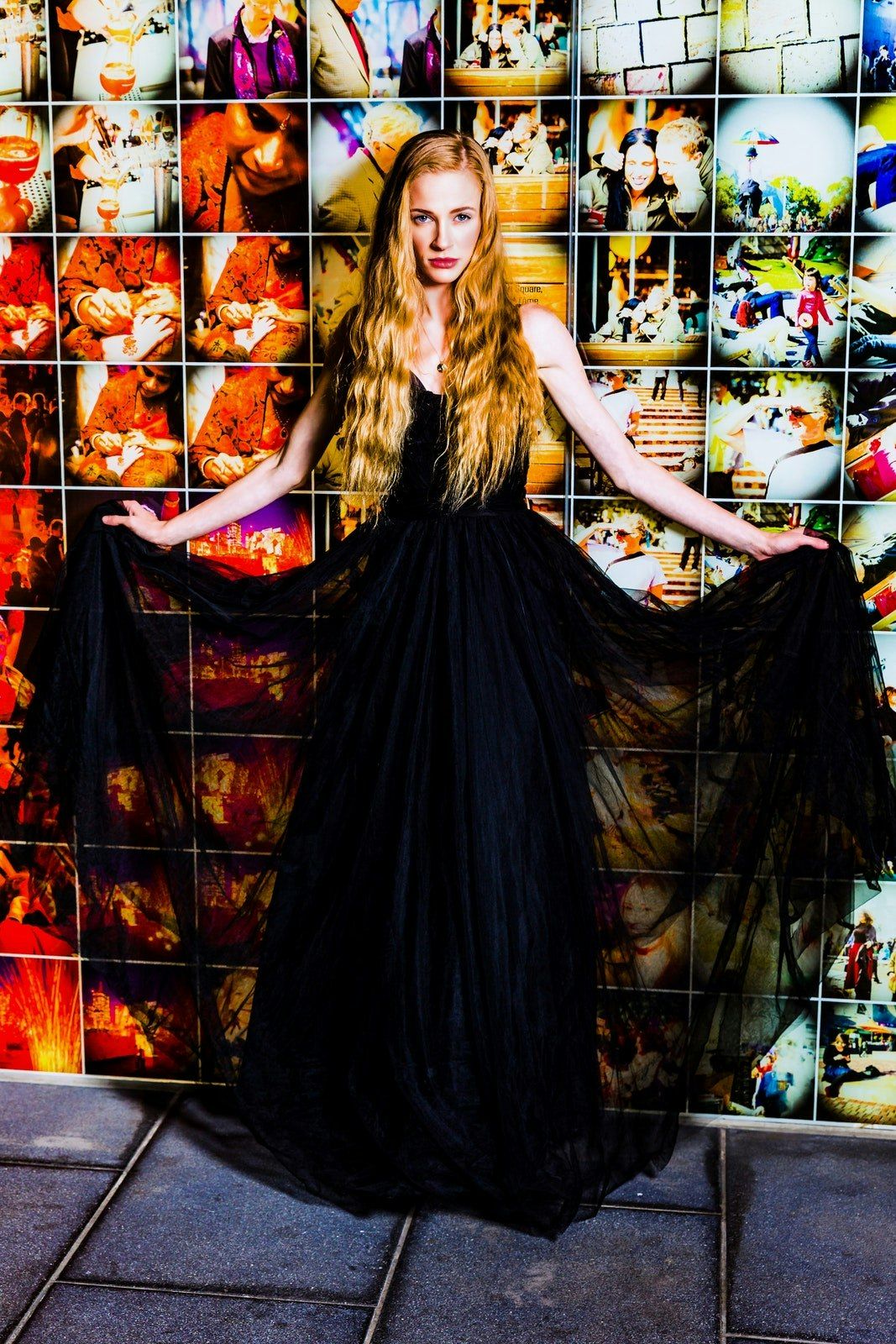 Dramatic fashion series in black dress against colorful mosaic wall background.