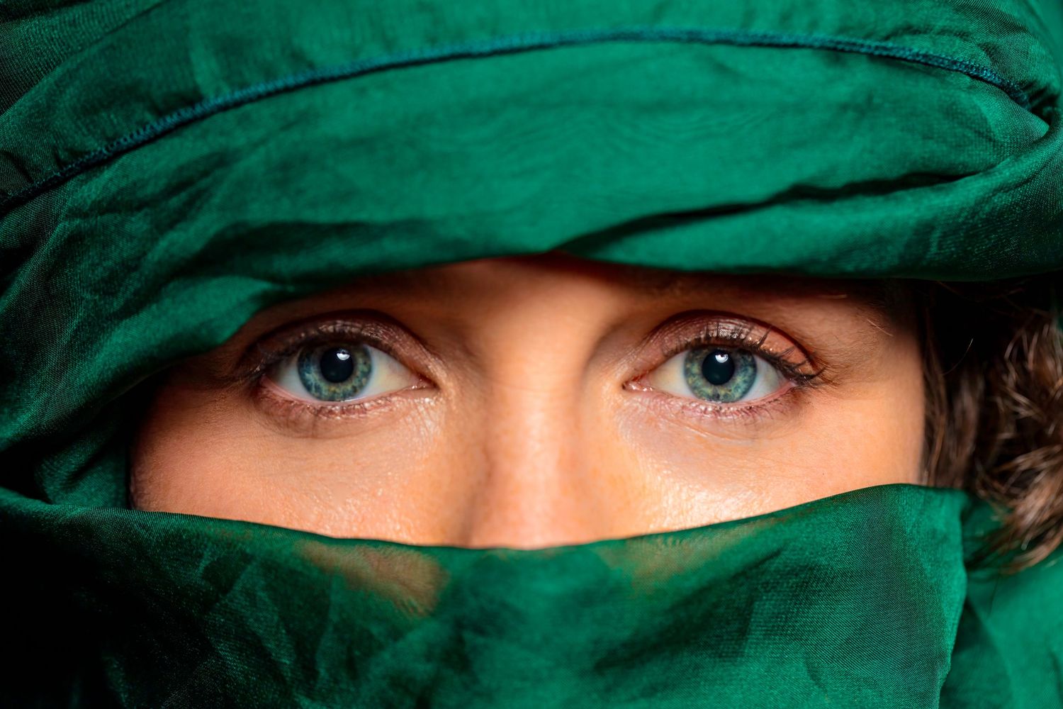 Close-up of striking blue eyes framed by a green fabric veil covering the face.