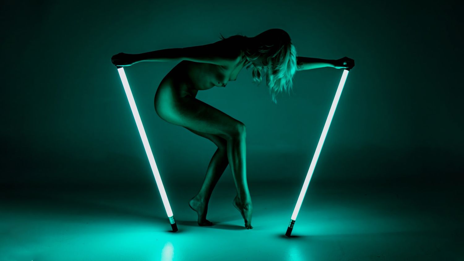 Silhouetted dance poses captured against neon turquoise lighting with geometric light patterns.