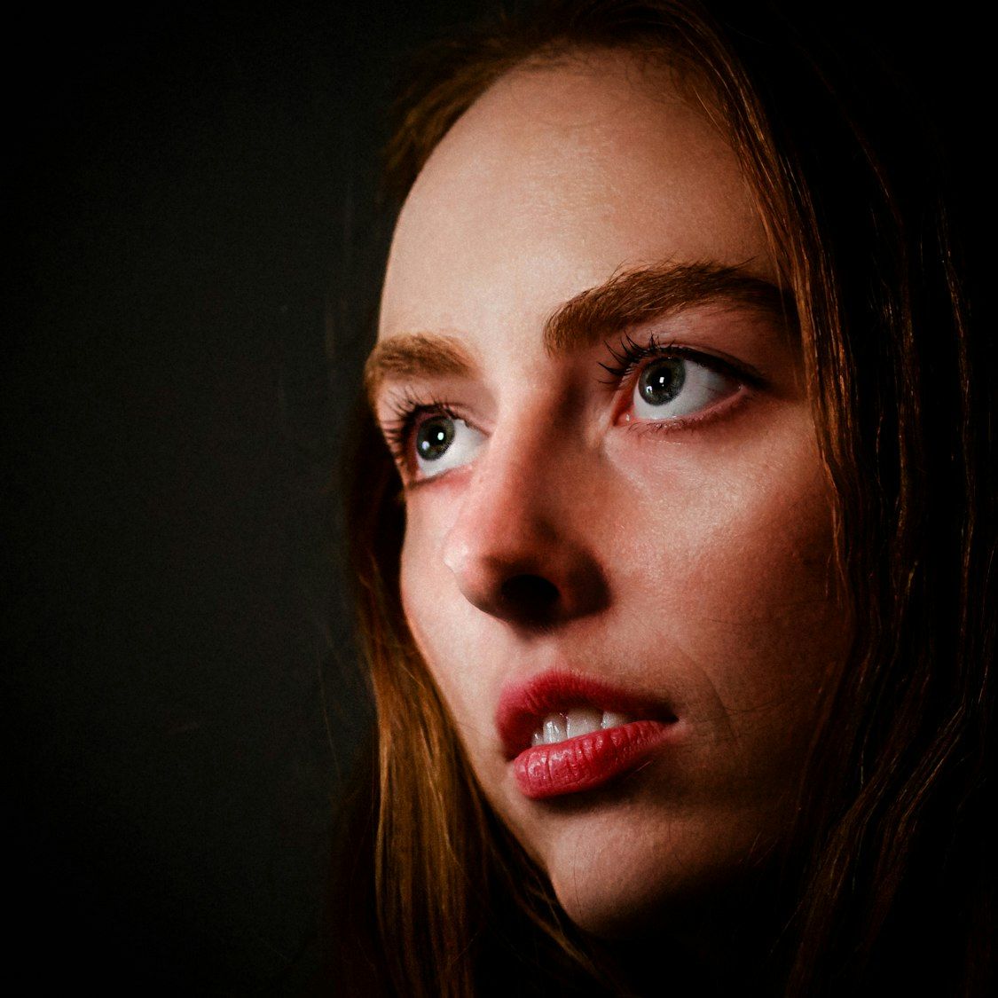 Close-up dramatic portrait with focus on red lipstick and side lighting.