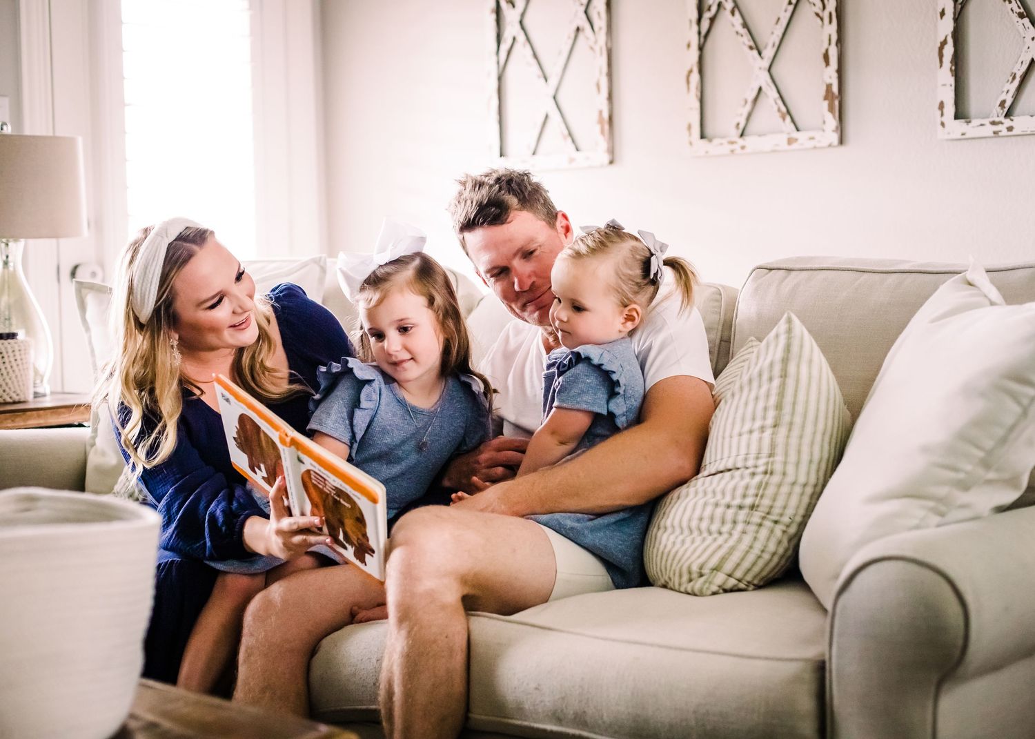 A family sits together on a gray couch reading a book and sharing a joyful moment in their living room.