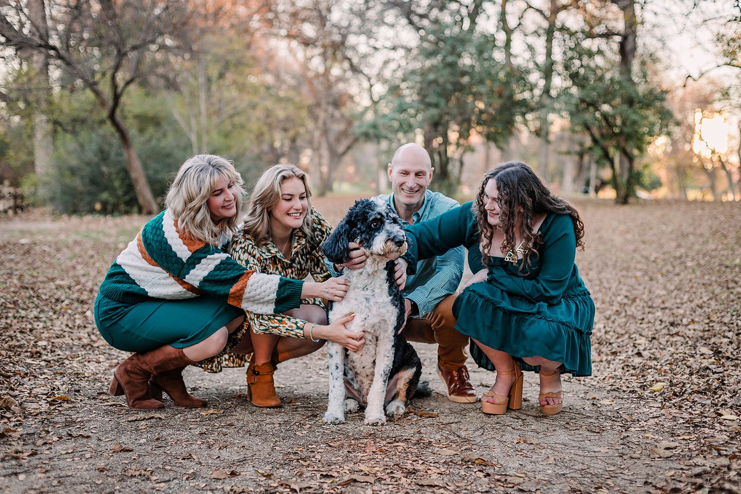 Group crouching to pet their black and white dog in a fall woodland setting.