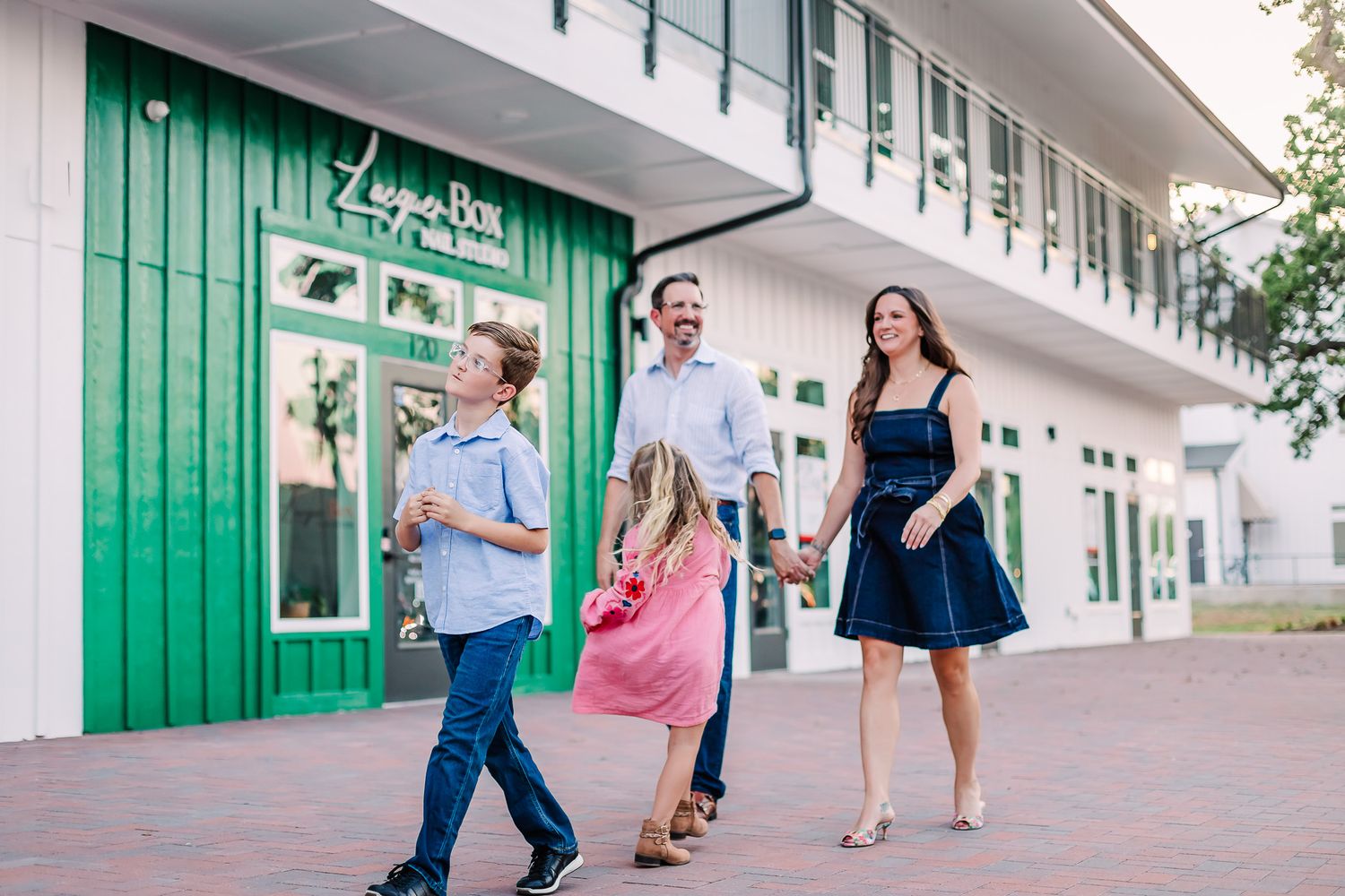 Family walking and interacting along modern shopping center exterior with green accents in downtown Arlington TX