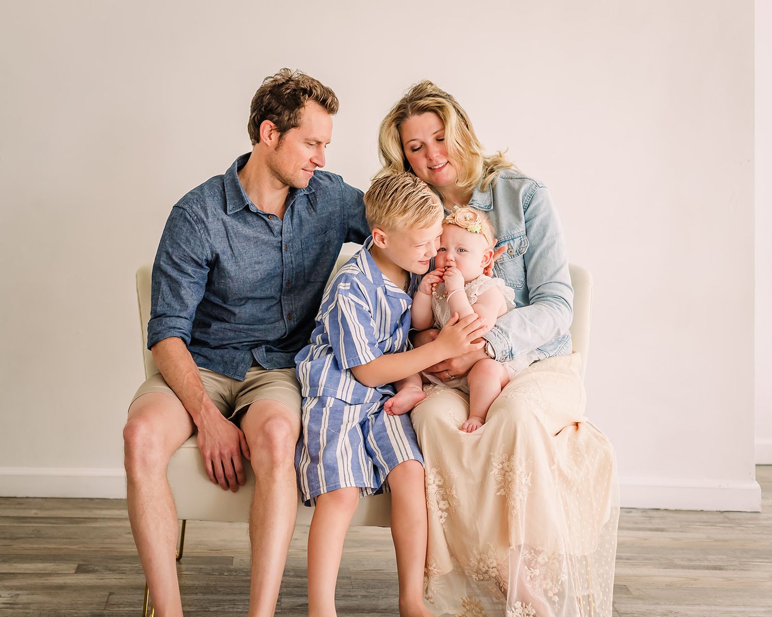 Family members sitting together on wooden bench in casual clothing against neutral background in candid poses.