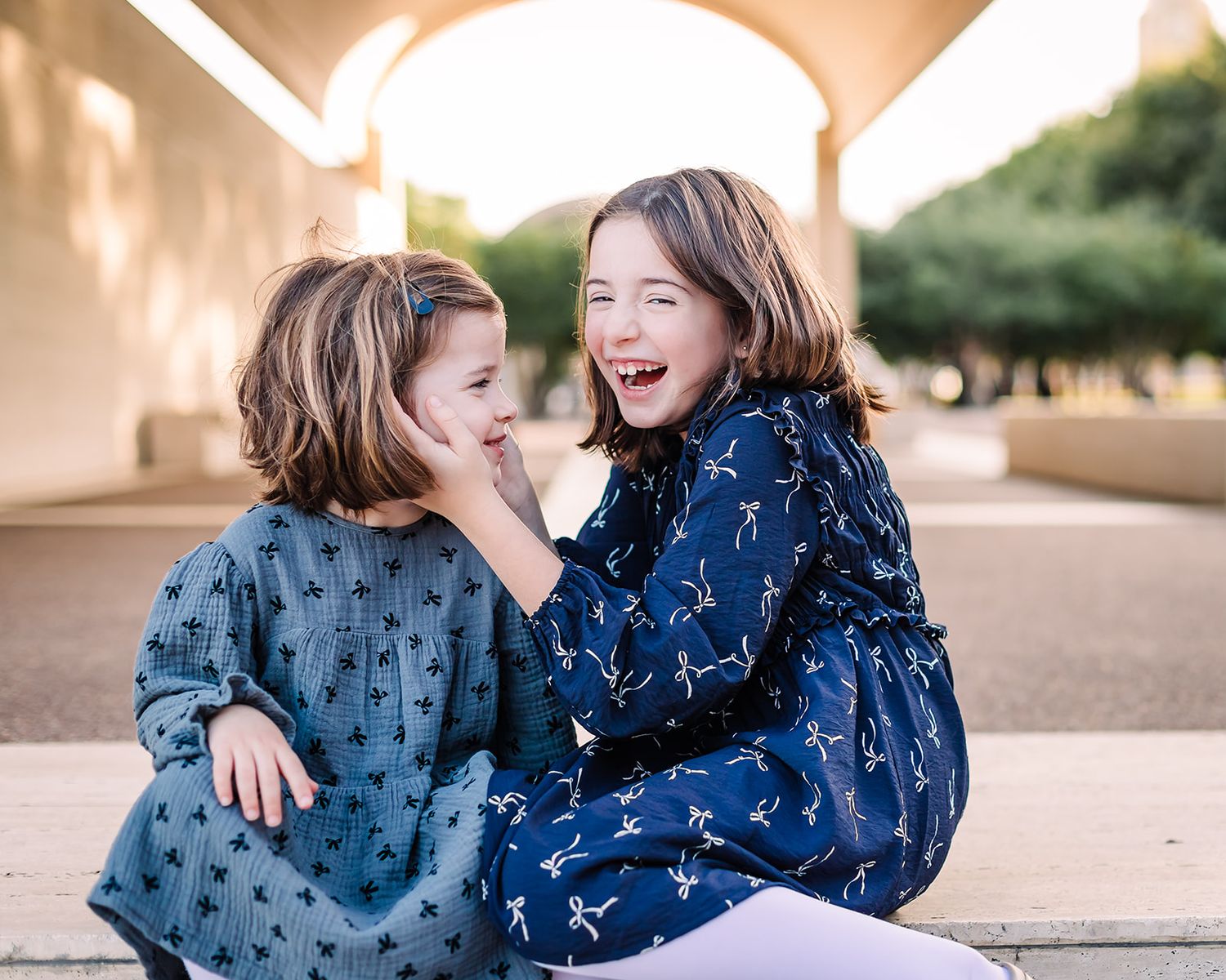 Two children in patterned outfits share joyful laughter while sitting together.