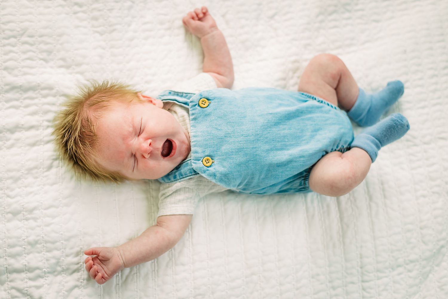 A baby in a teal onesie lies on a white blanket showing different emotional expressions in a series of photos.