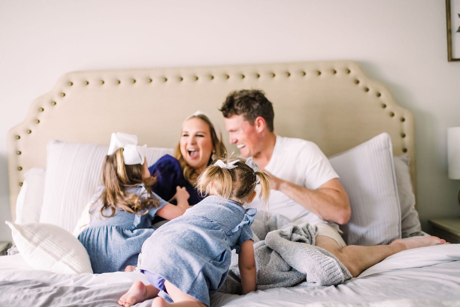 Family sharing intimate moments together on a white bed in natural light.
