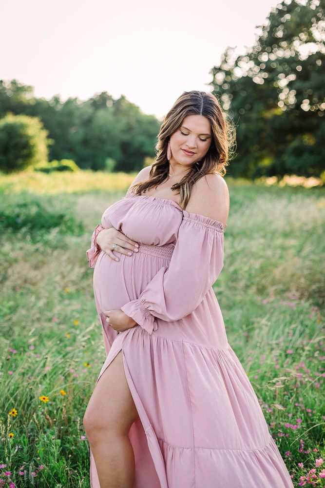 Woman in pink dress poses gracefully in sunlit meadow during maternity photoshoot in Dallas TX