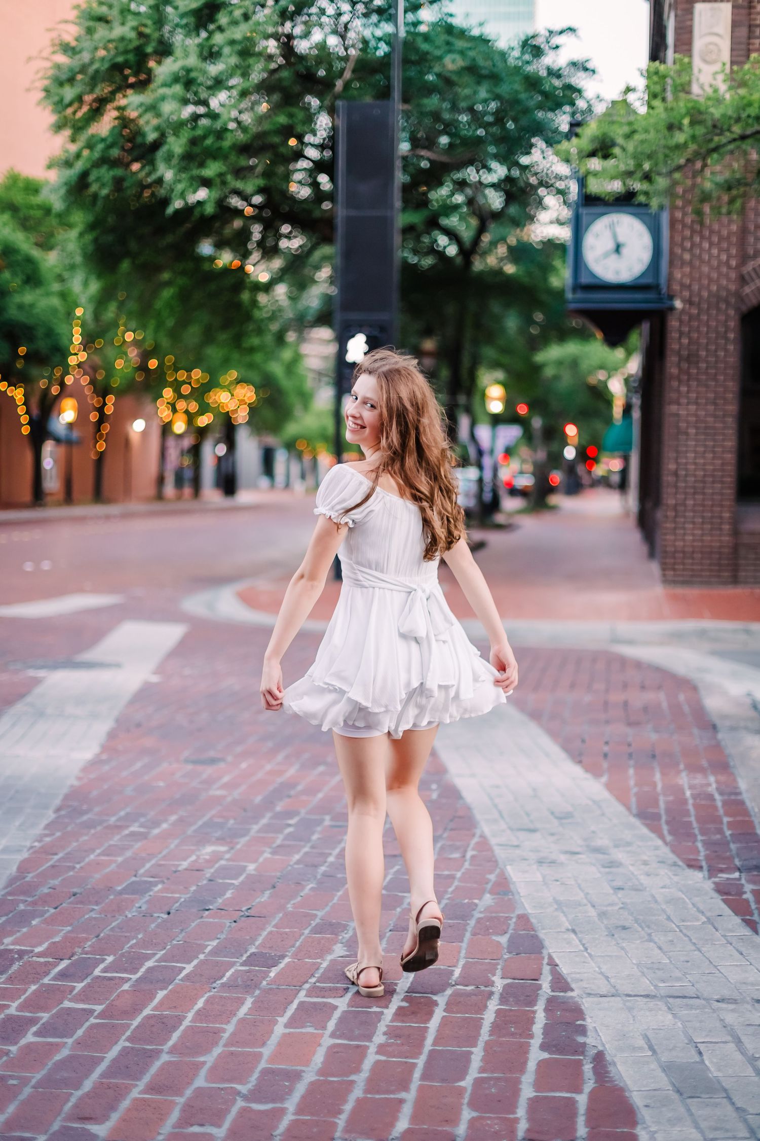 Child in white dress twirling and dancing on brick sidewalk downtown.