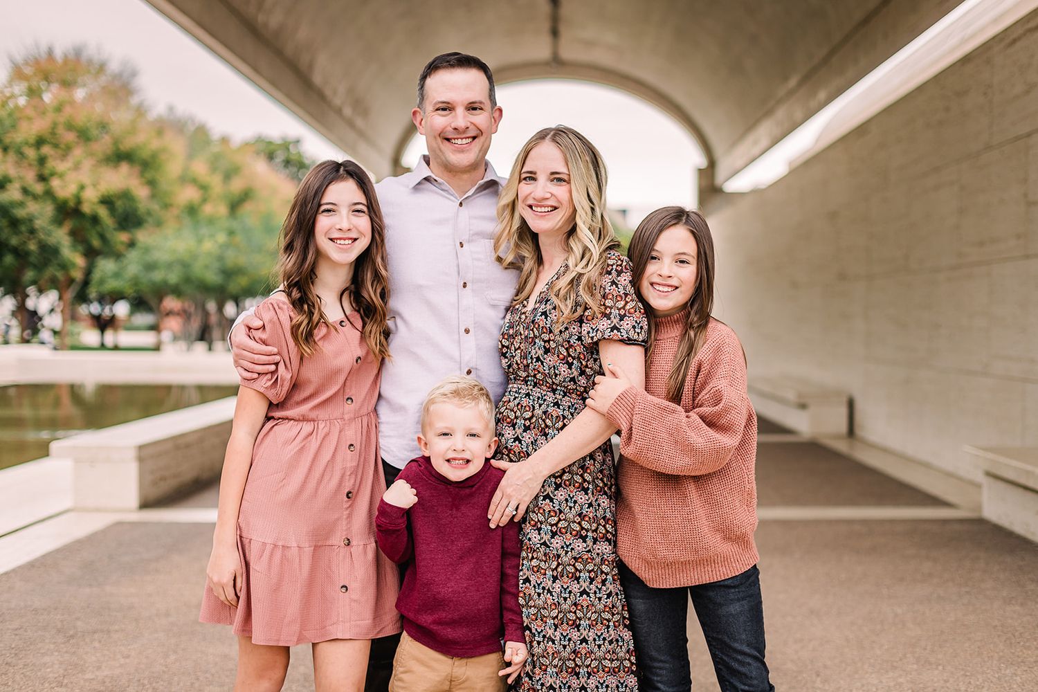 Family portrait session under a concrete bridge with warm autumn colors in their outfits.