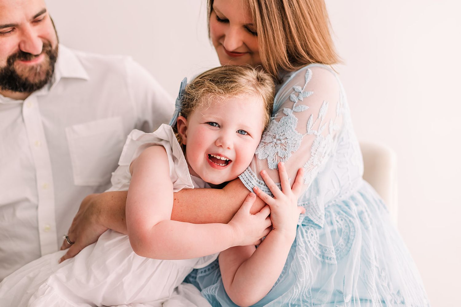 A tender family moment captured in soft lighting against a white background.
