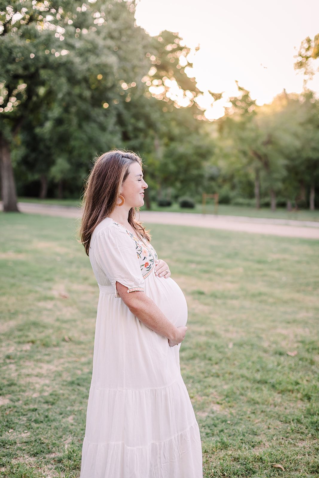 A woman in a white dress poses in a grassy field during golden hour.