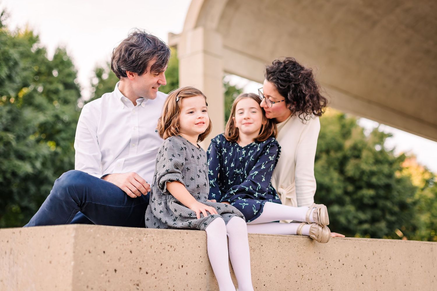 A family of four sits together and laughs on a concrete ledge under an archway.