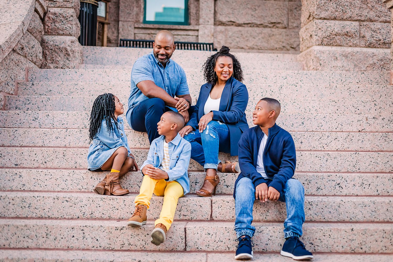 Three people sitting on stone steps wearing casual blue outfits and having a relaxed conversation together.