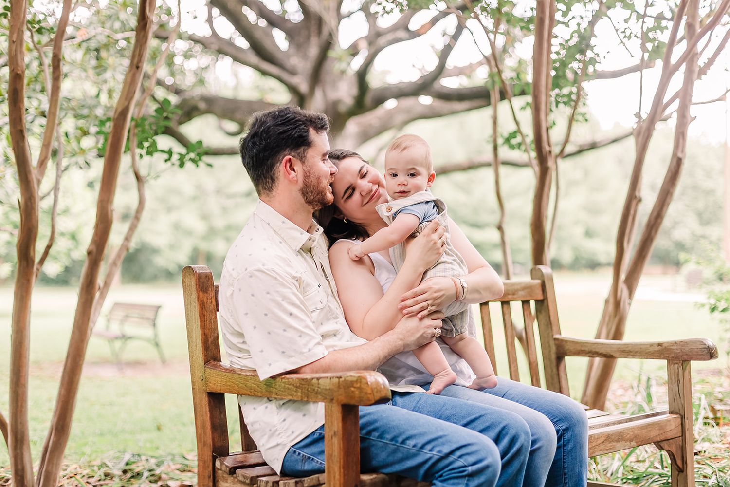 Family relaxing together on wooden bench under shady trees.