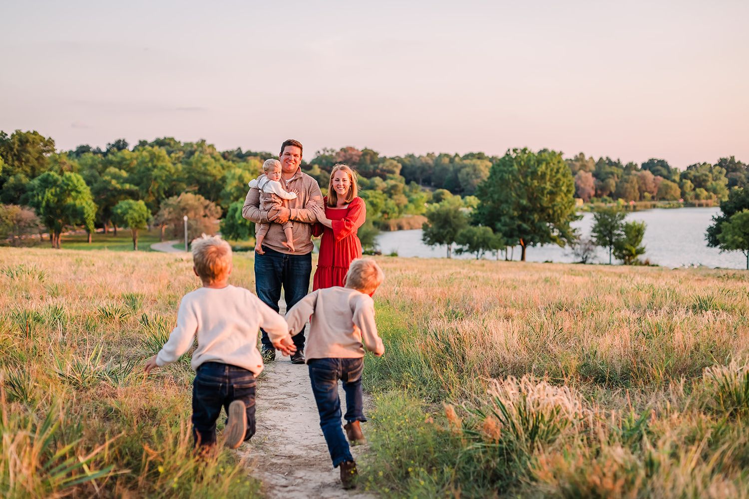 Family running and playing together on a path through a scenic meadow at sunset.
