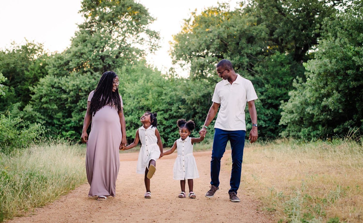 A family walking together through a grassy meadow during golden hour, captured in a panoramic style photograph.
