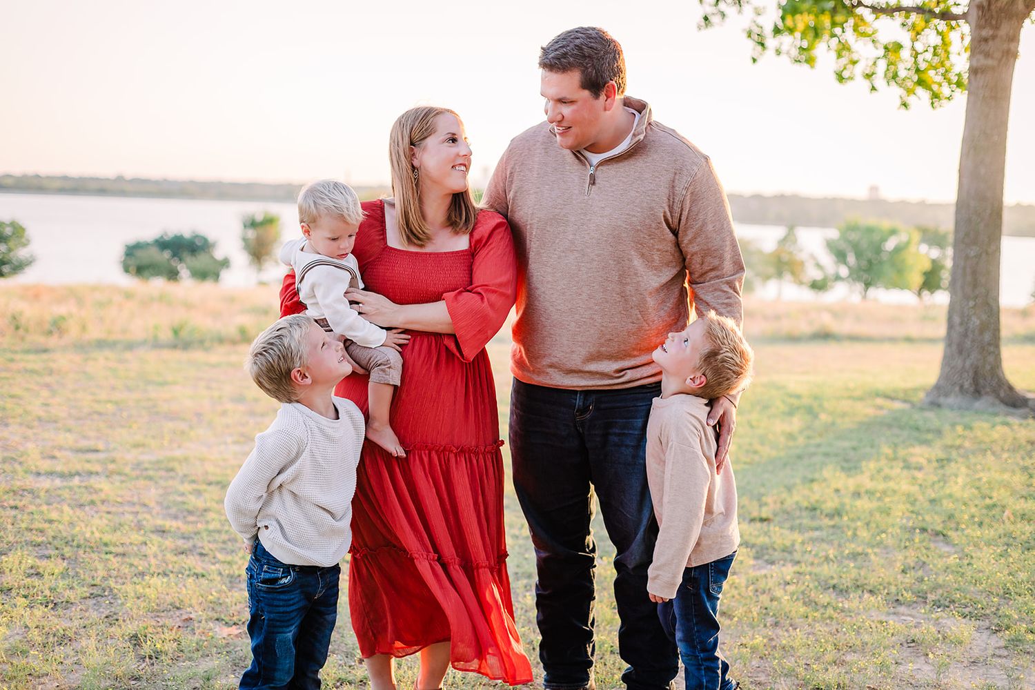 Family in coordinated red and neutral outfits posing together in a sunlit field.