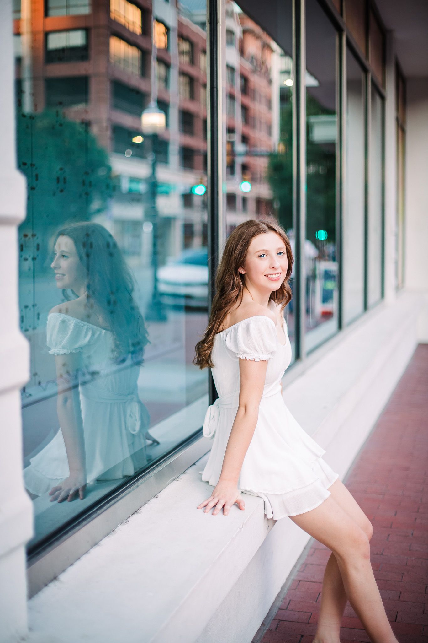 A person in a white summer dress leans against a storefront window with their reflection visible in the glass in sundance square fort worth