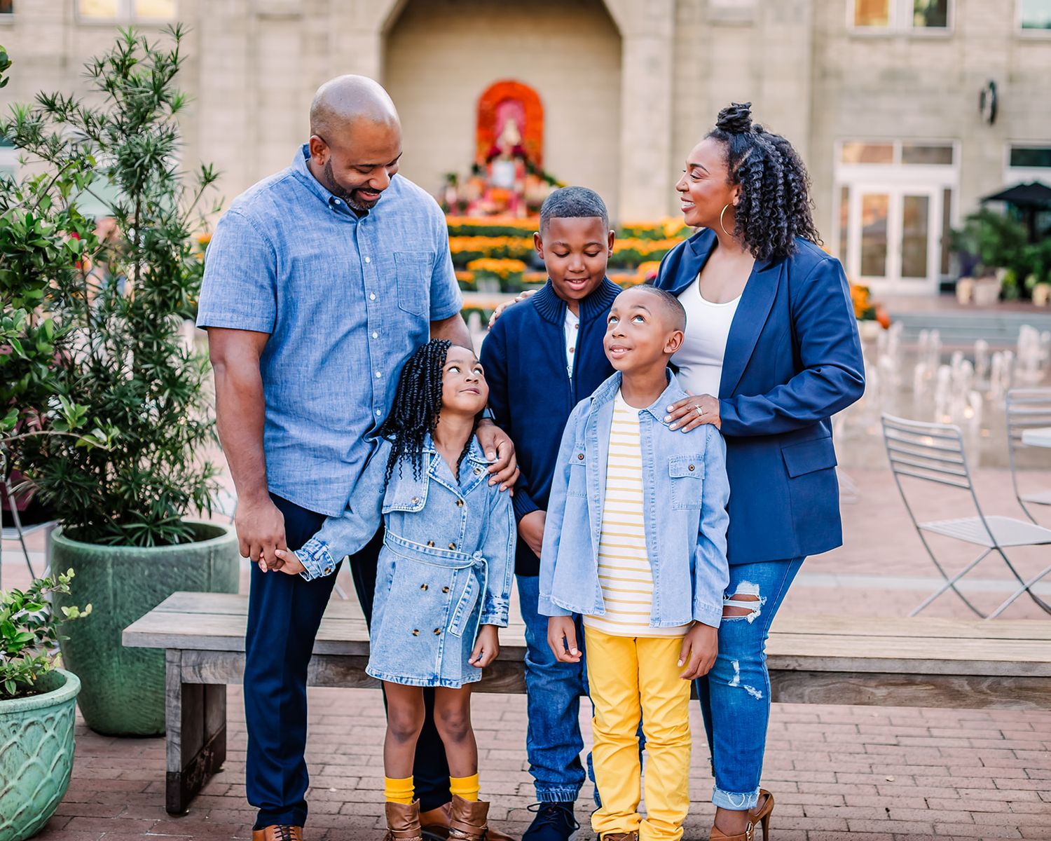 A family in coordinating blue and yellow outfits walks together on a stone paved path near a garden.