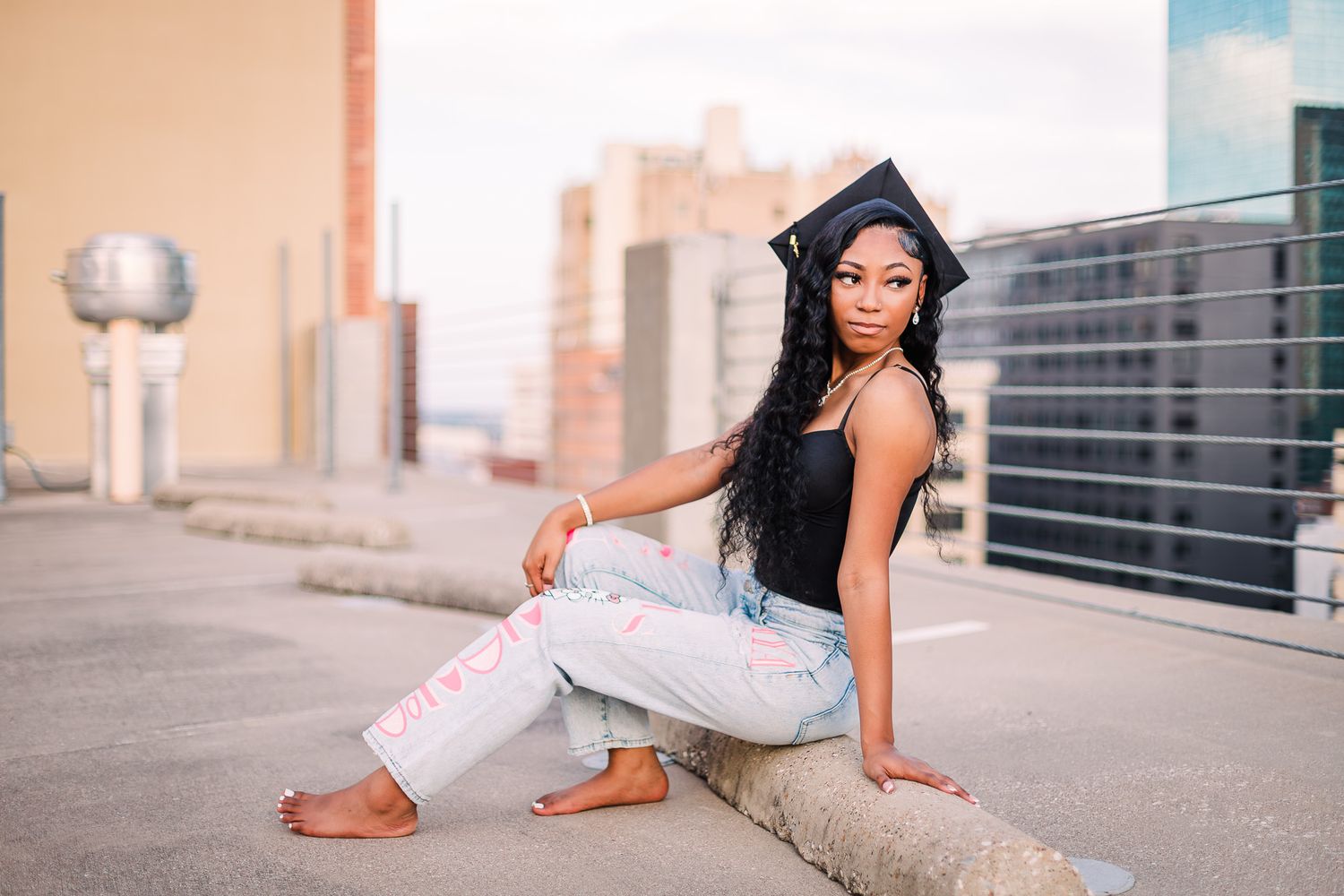 A high school senior in light colored pants and a black top poses on an urban sidewalk in different relaxed positions on garage rooftop TX