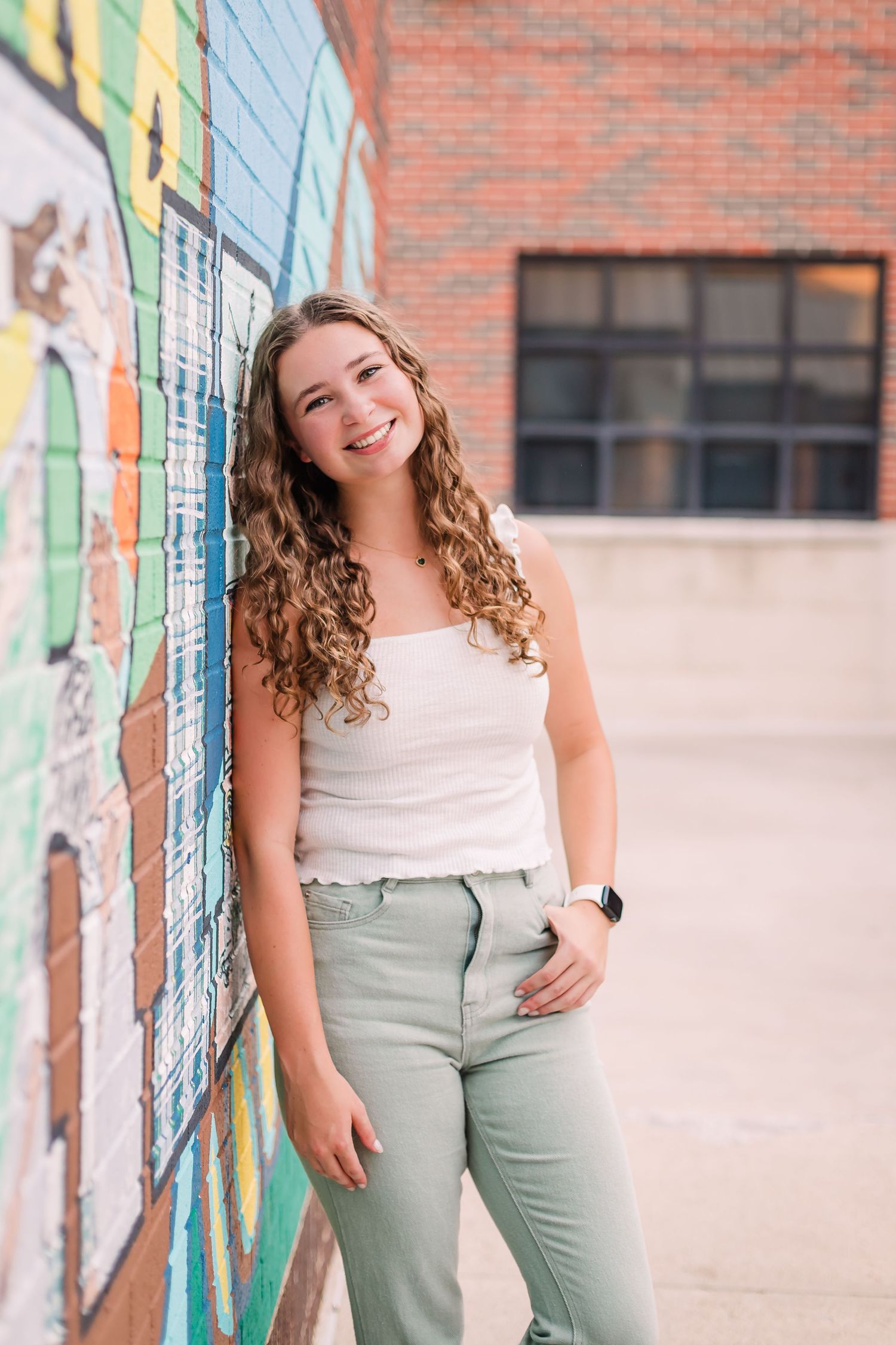 Casual portraits against a colorful graffiti wall wearing white top and sage green pants.