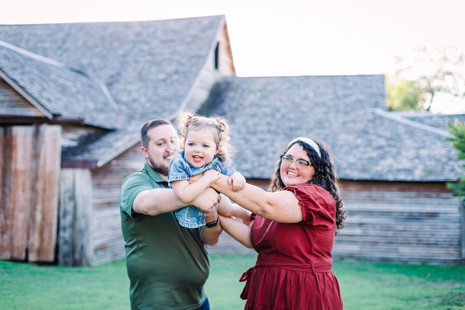 People interacting playfully against a rustic barn backdrop during an outdoor photoshoot.