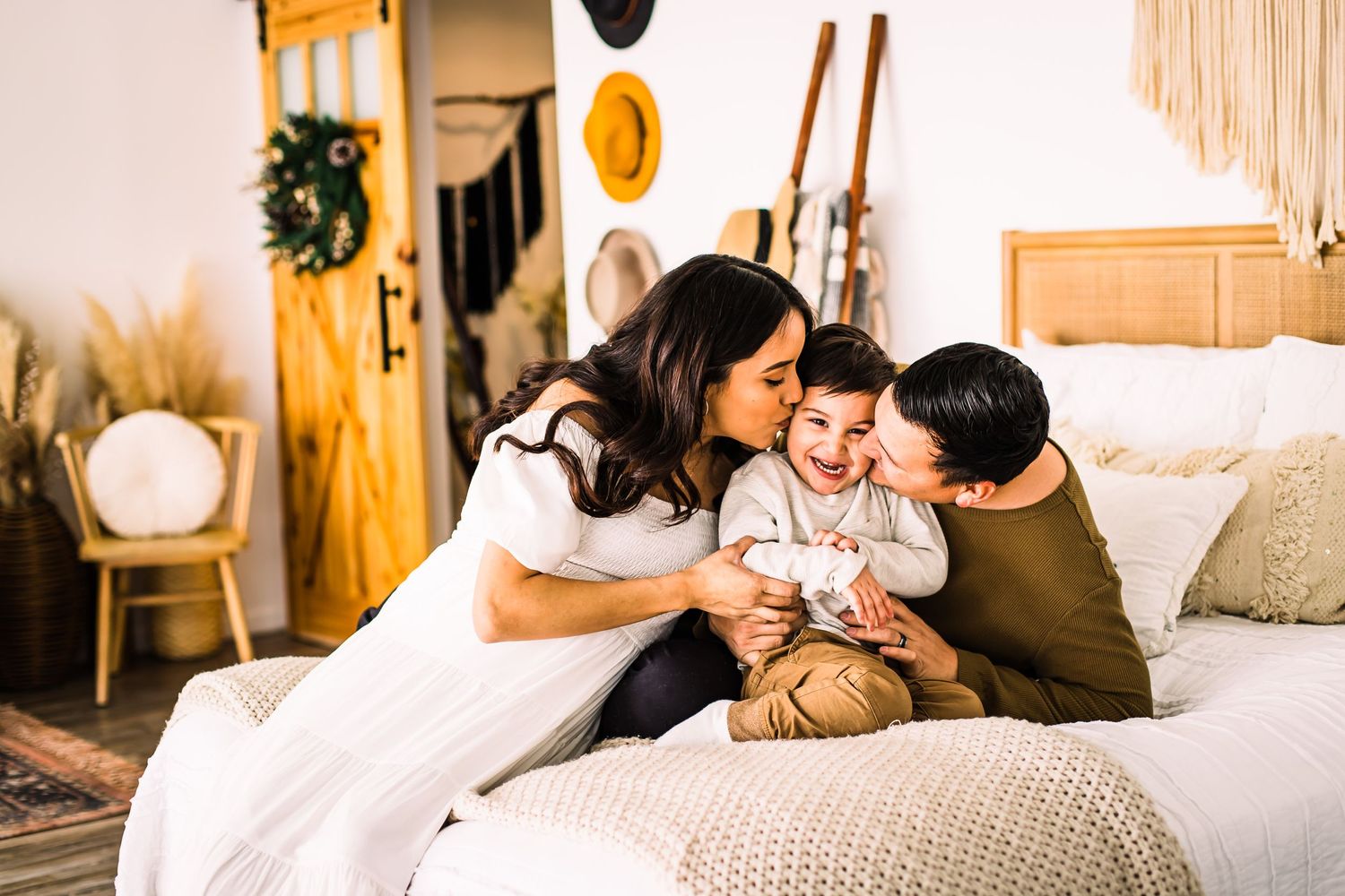 parents kissing child on cheek in bed maternity photoshoot