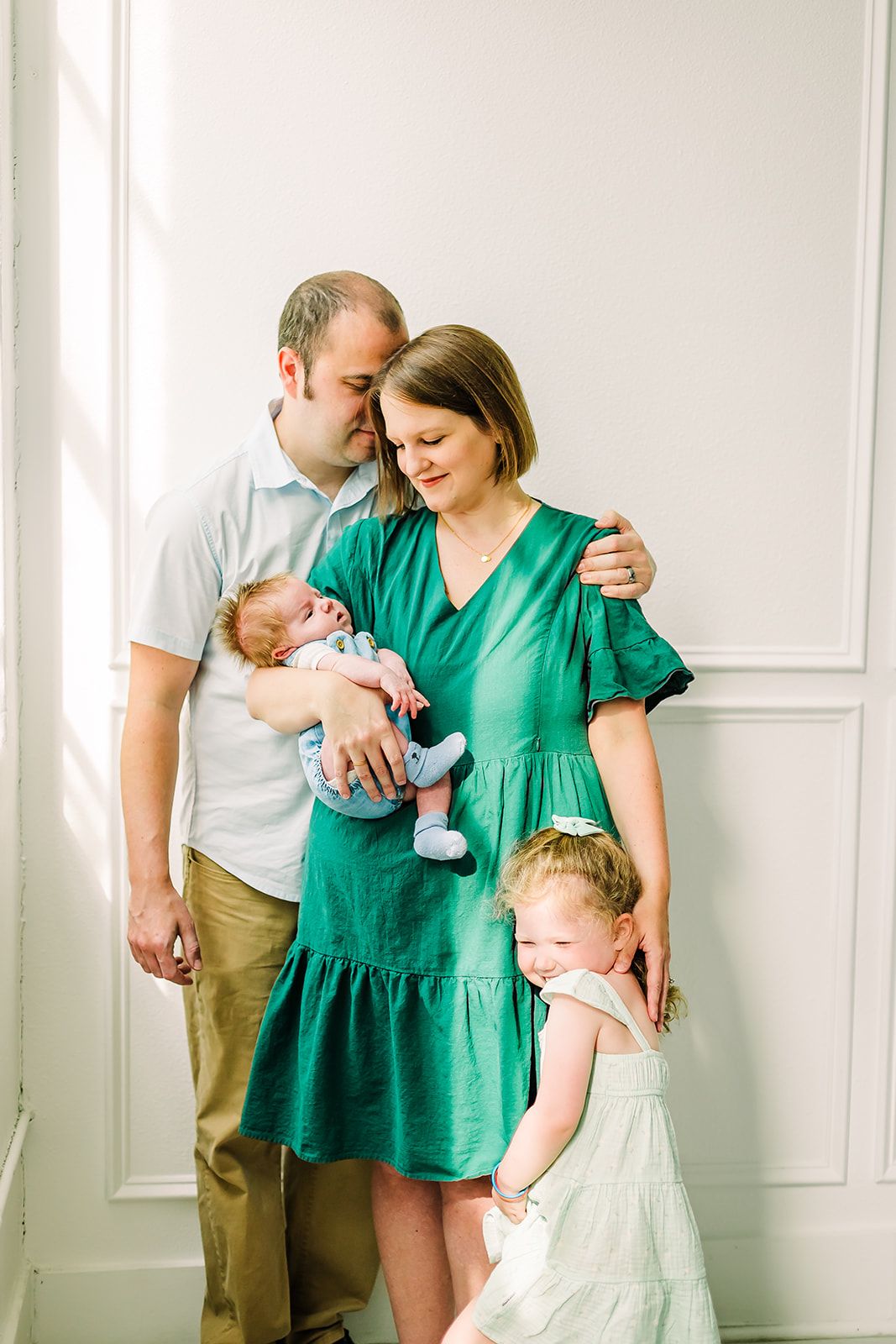 A family shares tender moments together in a bright white room with a baby.